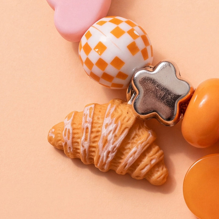BEADBOO Butter Croissant charm hanging on a handmade beaded dog collar [crop:charm-croissant-baked__javier]